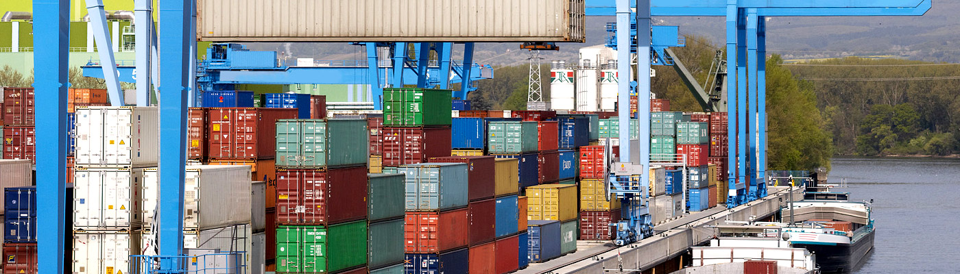 Eine Hafenansicht mit zahlreichen bunten Containern, Kränen und einem Fluss.